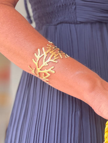 brazalete de mujer dorado con diseño de coral colocado en el antebrazo