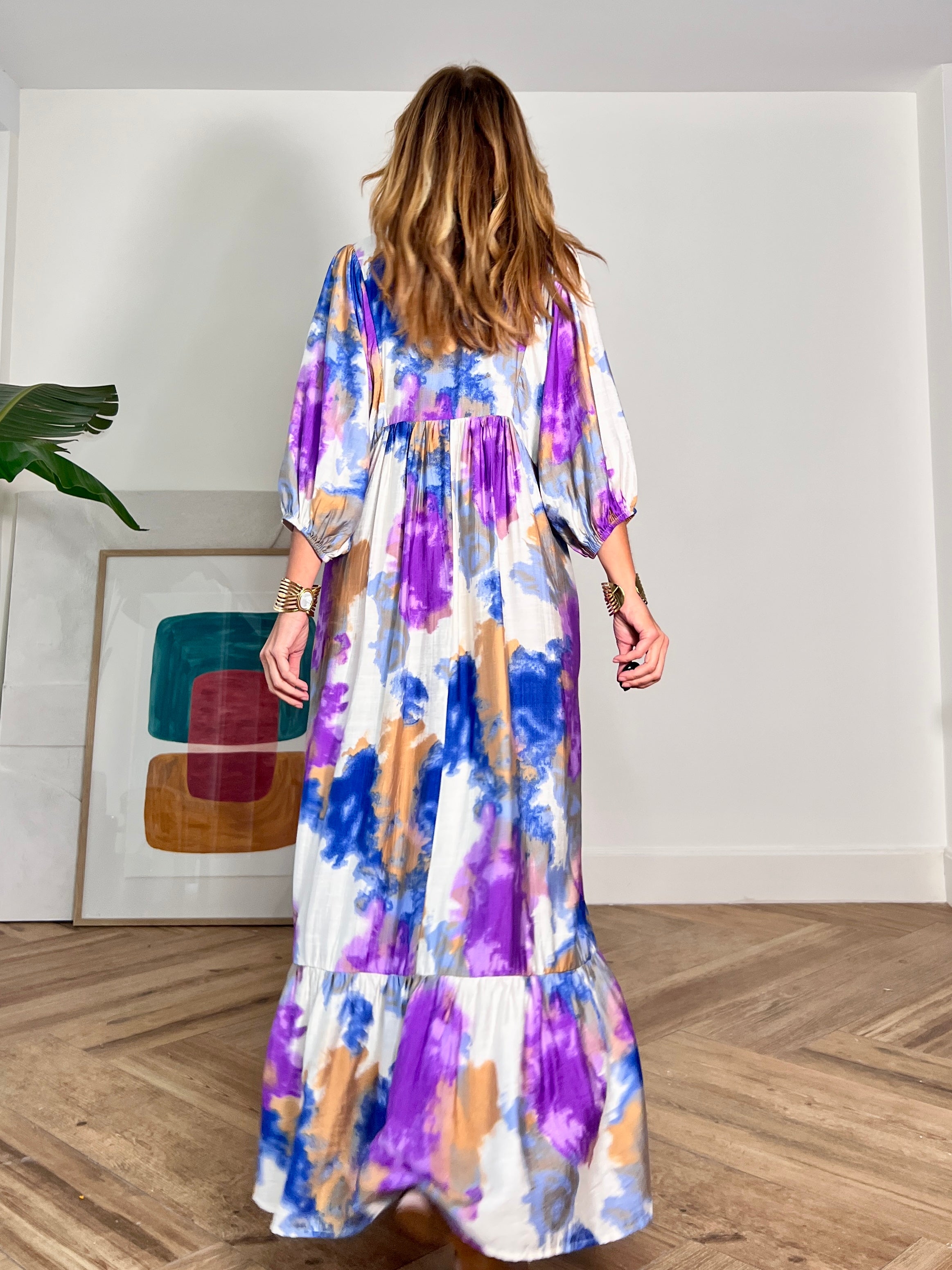 Espalda de vestido largo y fluido en estampado lila, azul y blanco , con amplias mangas y volante  fluido.